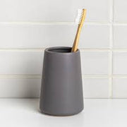Gray toothbrush holder with a wooden toothbrush on a white surface and tiled wall background