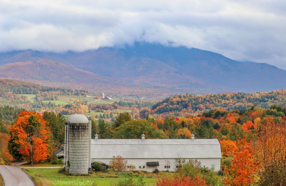 Farm with barn and silo surrounded by autumn trees and mountains in the background